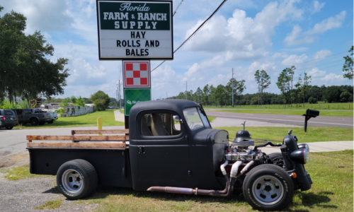 A black rat rod parked in front of the Florida Farm & Ranch Supply store sign.